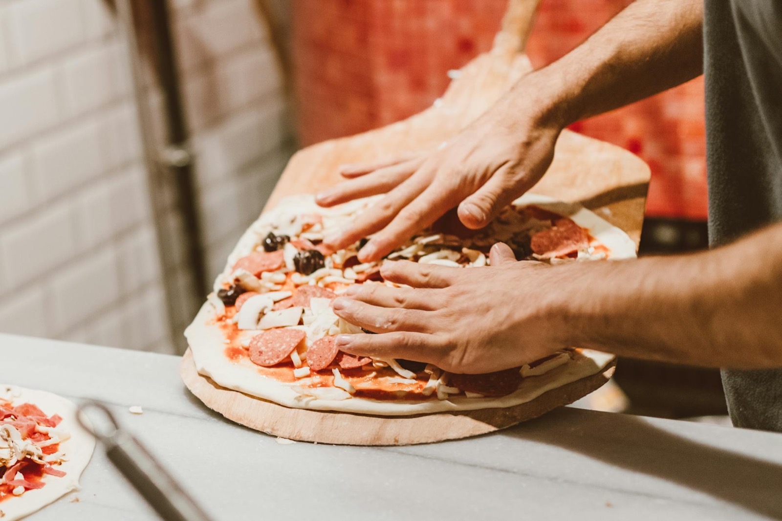 Dłonie pizzaiolo układają składniki na rozciągniętym cieście